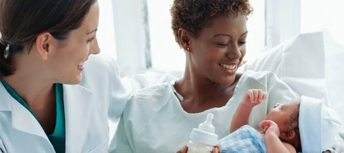 A new mother smiling with her baby, supported by a caregiver